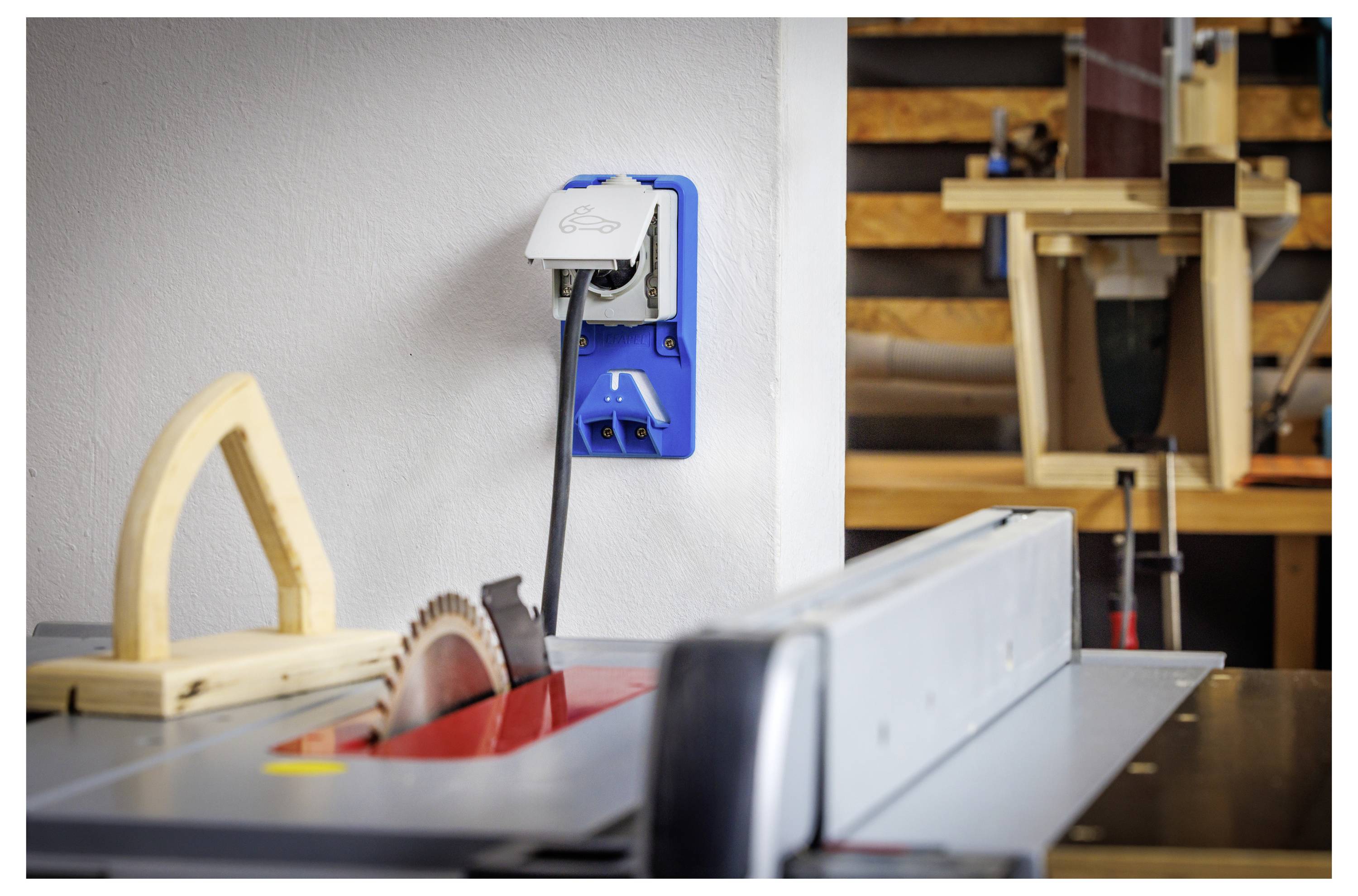 Werkstatt-Tischkreissäge mit Blatt und Zaun im Vordergrund, Steckdose und angestöpseltes Kabel an der Wand, Holzbearbeitungswerkzeuge und Projekte im Hintergrund.