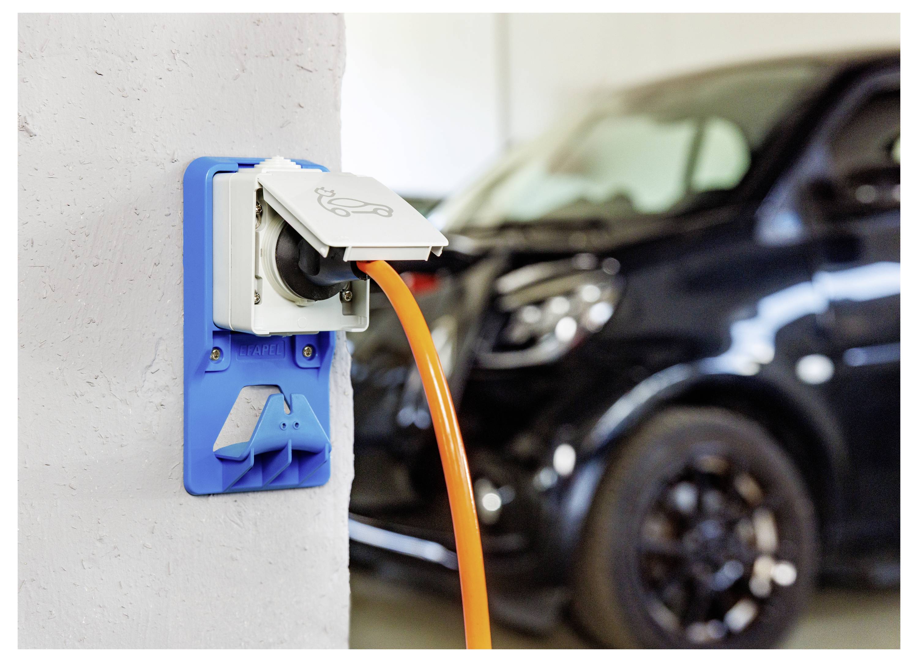 Elektrofahrzeug-Ladekabel in eine wandmontierte Ladebuchse gesteckt, mit einem Auto im Hintergrund geparkt.