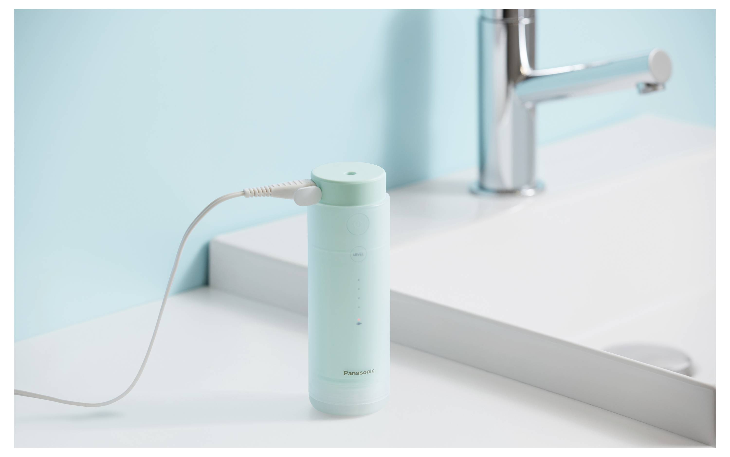 Mintgrüne elektrische Zahnbürste lädt neben einem Waschbecken und Wasserhahn im Bad auf einer weißen Arbeitsplatte auf.