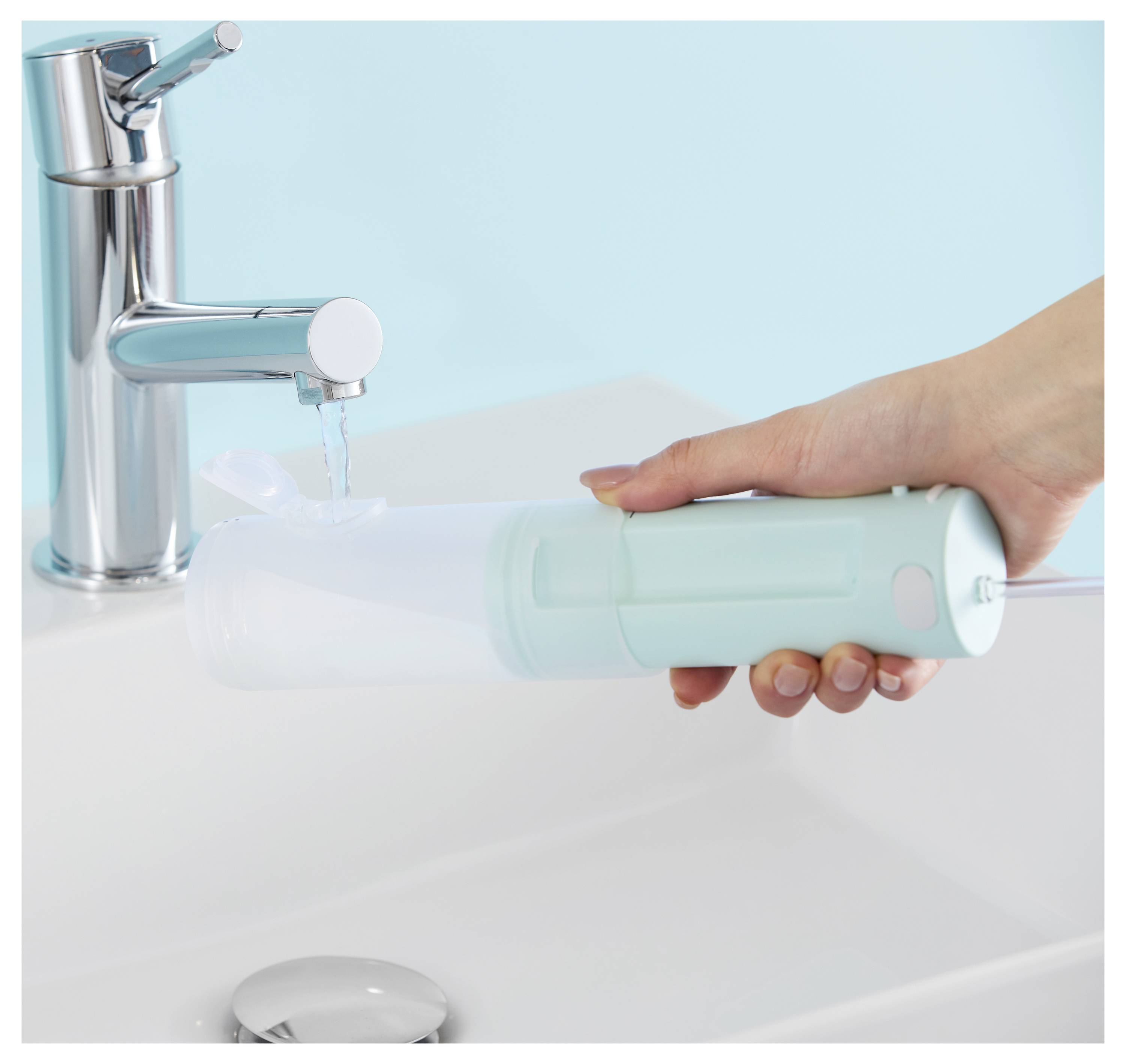 Eine Hand, die einen tragbaren Wasserflosser unter einem laufenden Wasserhahn über einem Waschbecken hält, um ihn mit Wasser zu füllen.