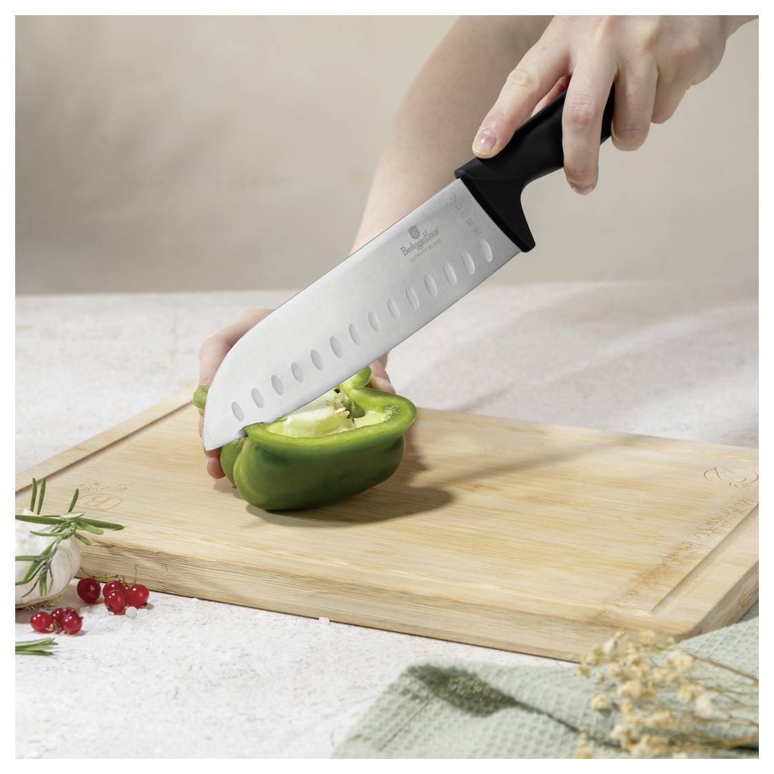 Hände schneiden eine grüne Paprika auf einem Holzschneidebrett mit einem Kochmesser.