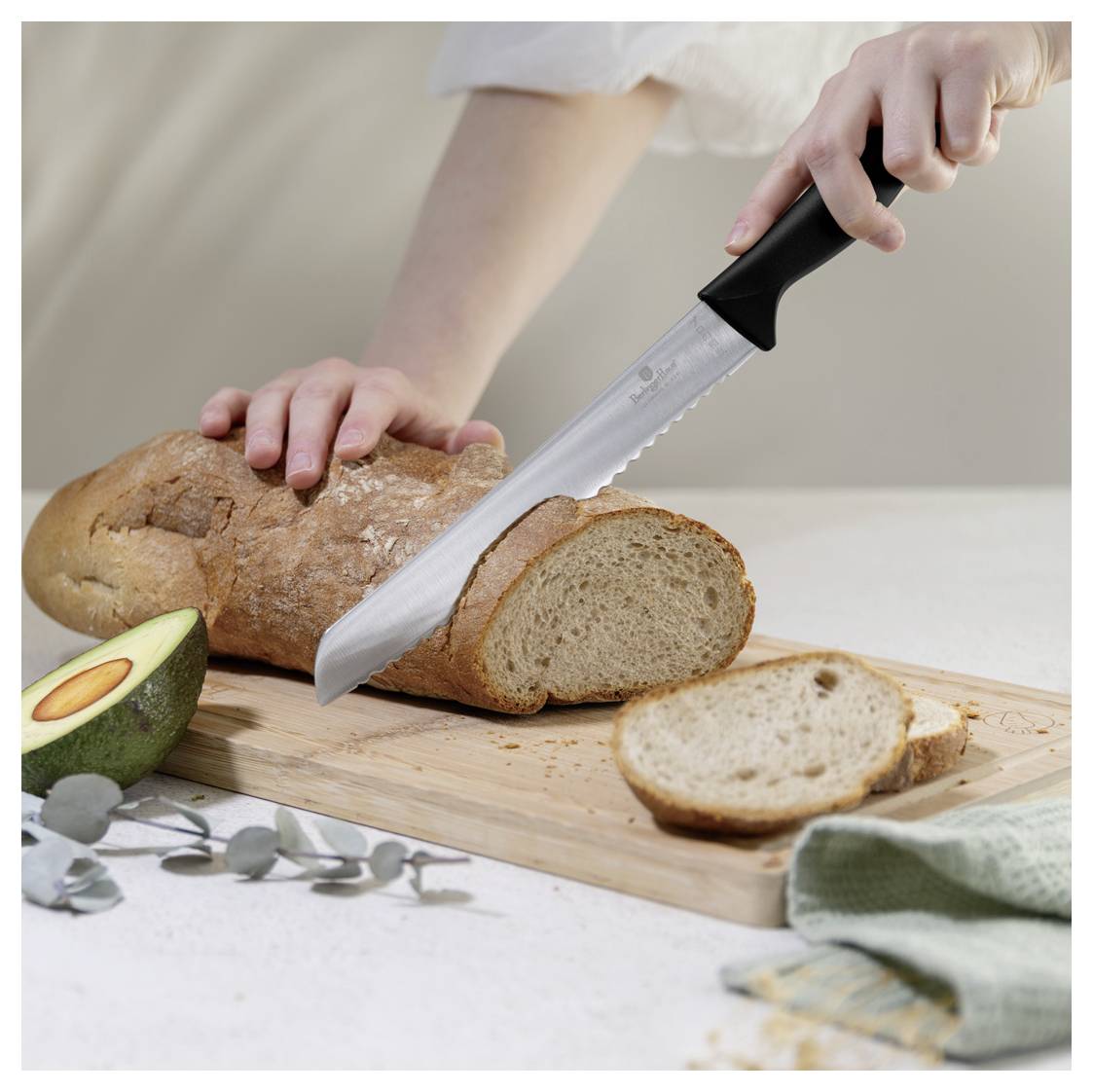 Hände schneiden ein Brotlaib auf einem Schneidebrett, wobei ein Stück bereits abgeschnitten ist und eine Avocado in der Nähe liegt.