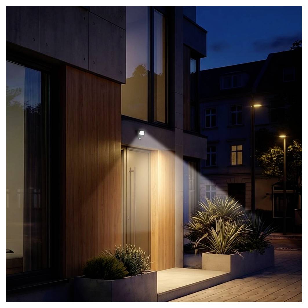 Moderner Apartmenteingang in der Dämmerung, warm beleuchtete Eingangstür mit Holz- und Glaselementen, Blumenkübel und stille Straße draußen.