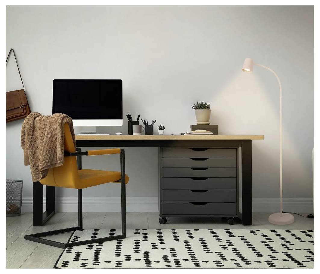 Minimales Homeoffice mit gelbem Stuhl, Schreibtisch, Computer, Schubladen, Stehleuchte und gemustertem Teppich vor einer einfachen Wand.