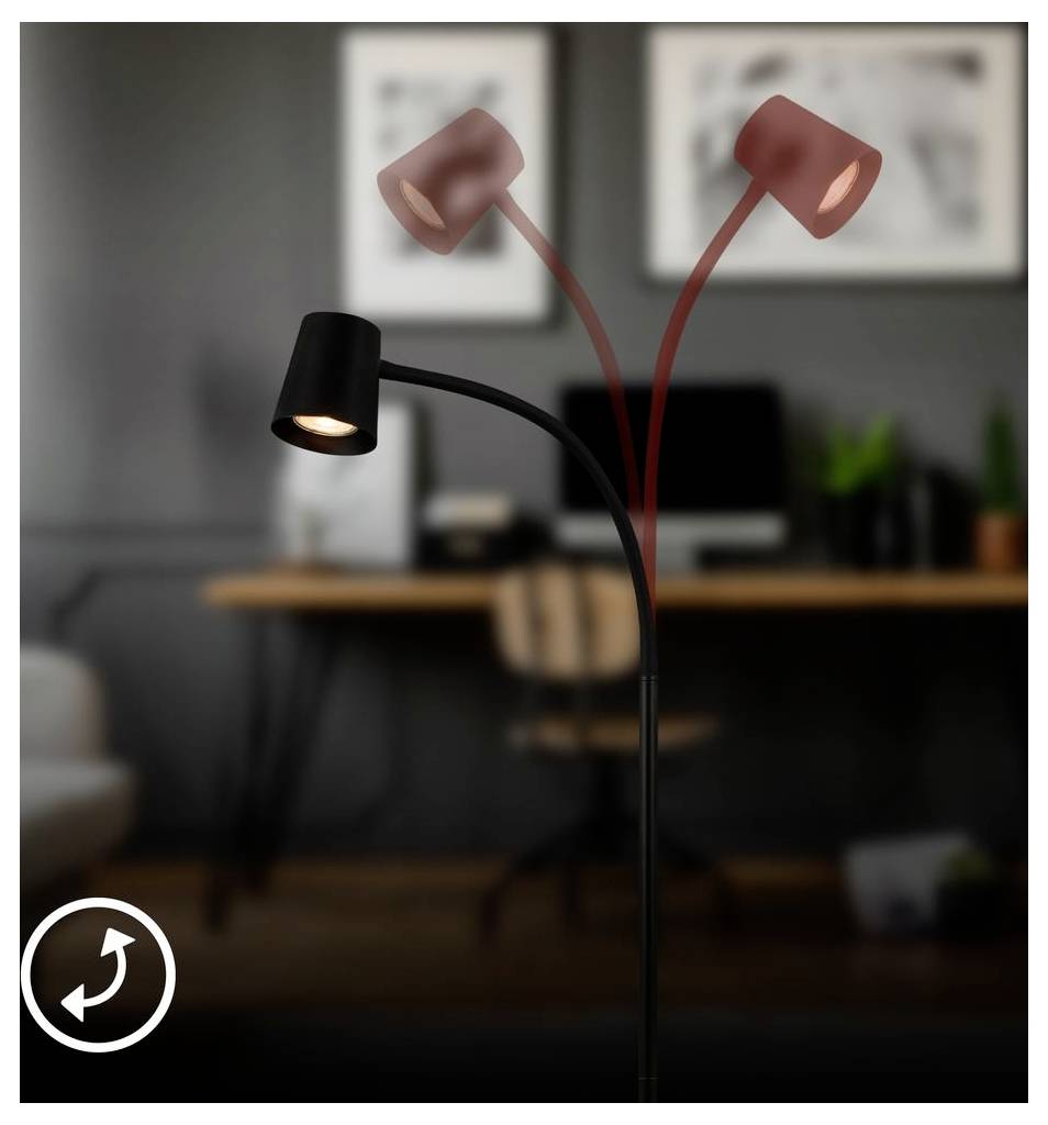 Schwarze verstellbare Schreibtischlampe mit zwei rotgefärbten Köpfen, einer davon leuchtet, im unscharfen Hintergrund eines Heimbüros mit Schreibtisch und Stuhl.