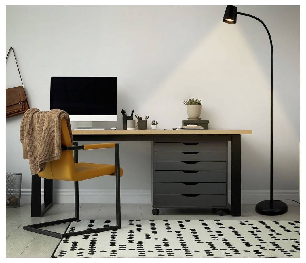 Modernes Homeoffice mit einem Schreibtisch, Computermonitor, gelbem Stuhl mit drapierter Decke, Stehlampe und gemustertem Teppich.