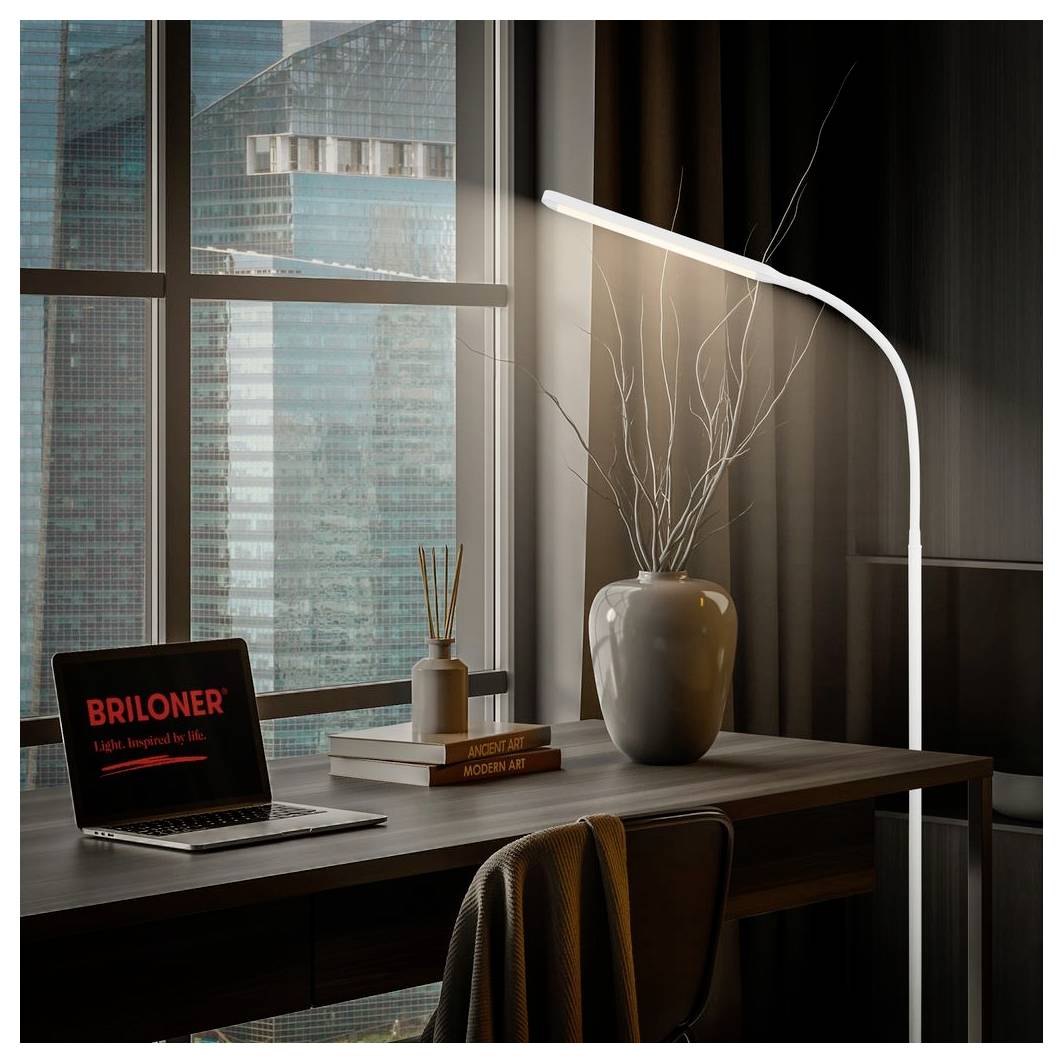 Modernes Homeoffice mit Laptop, Schreibtischlampe, Vase und Büchern neben einem Fenster mit Blick auf Stadtgebäude.