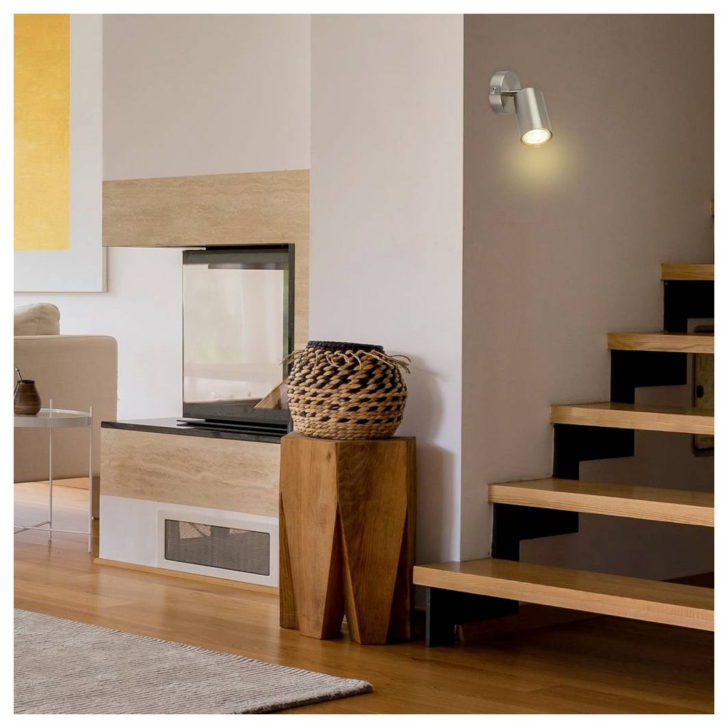 Moderne Wohnzimmerecke mit eingebautem Kamin, gewebtem Korb und Holztreppe, beleuchtet durch eine Wandleuchte.