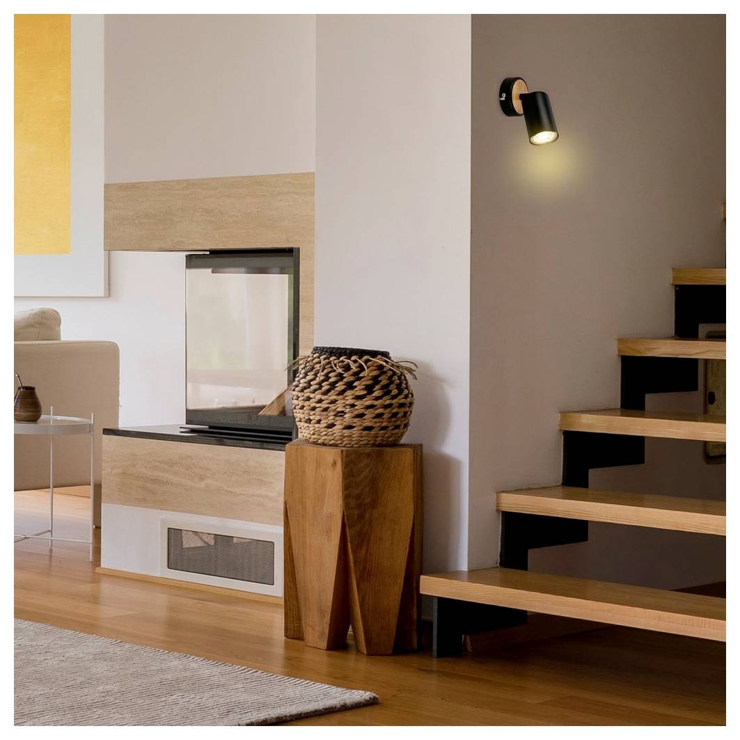 Modernes Wohnzimmer mit eingebautem Kamin, gewebtem Korb auf Holzständer und offener Holztreppe neben einer Wandleuchte.
