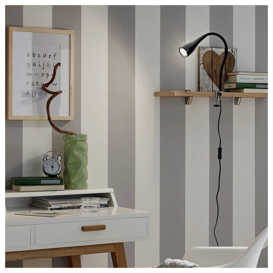 Stilvolle Arbeitszimmerecke mit gestreifter Tapete, gerahmter Buchstabengrafik, Schreibtischlampe, Regalen, Büchern, Uhr und dekorativer Vase.