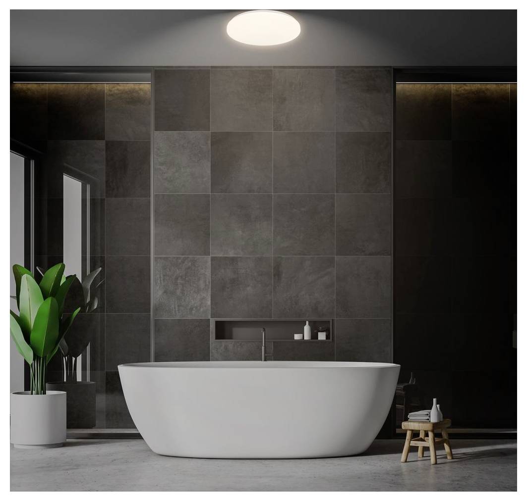 Modernes Badezimmer mit einer freistehenden weißen Badewanne, die vor dunklen gekachelten Wänden zentriert ist, beleuchtet durch eine Deckenleuchte, mit einer Topfpflanze und einem kleinen Hocker in der Nähe.