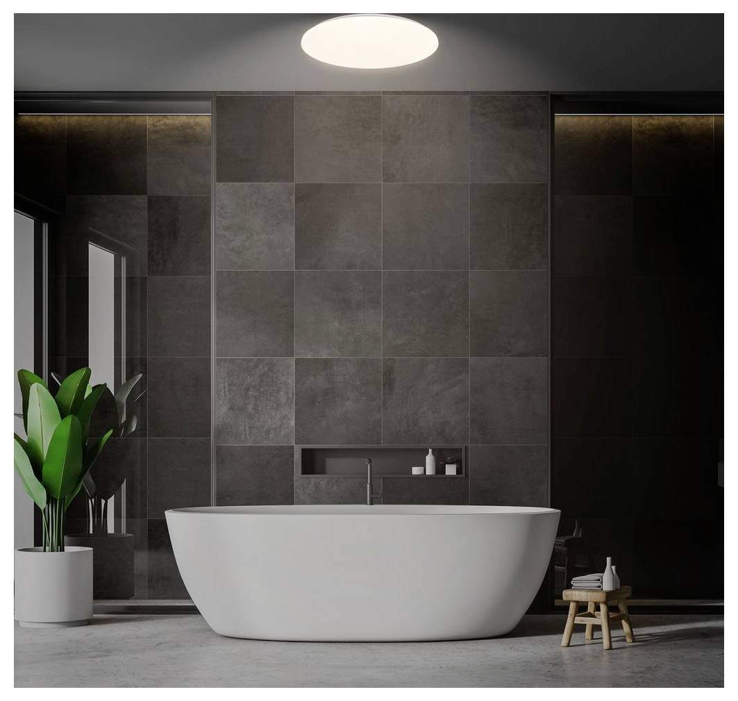 Modernes Badezimmer mit einer freistehenden weißen Badewanne, die vor dunklen gefliesten Wänden zentriert ist, beleuchtet durch eine Deckenleuchte und akzentuiert mit einer Topfpflanze und einem kleinen Hocker.