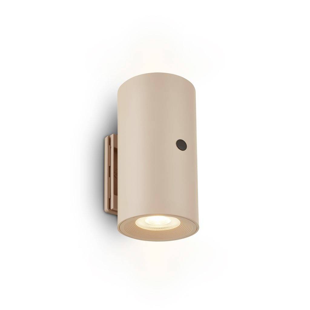 Beige-farbige zylindrische Wandleuchte mit eingeschaltetem, nach unten gerichtetem Scheinwerfer und kleinem schwarzem Schalter auf weißem Hintergrund.