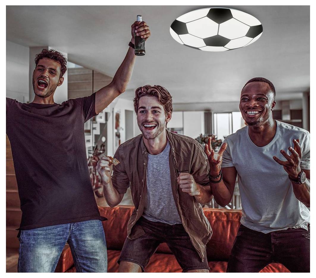 Drei Männer jubeln auf einem Sofa, einer hält eine Flasche hoch, während sie sich ein Fußballspiel im Fernsehen im Wohnzimmer ansehen.