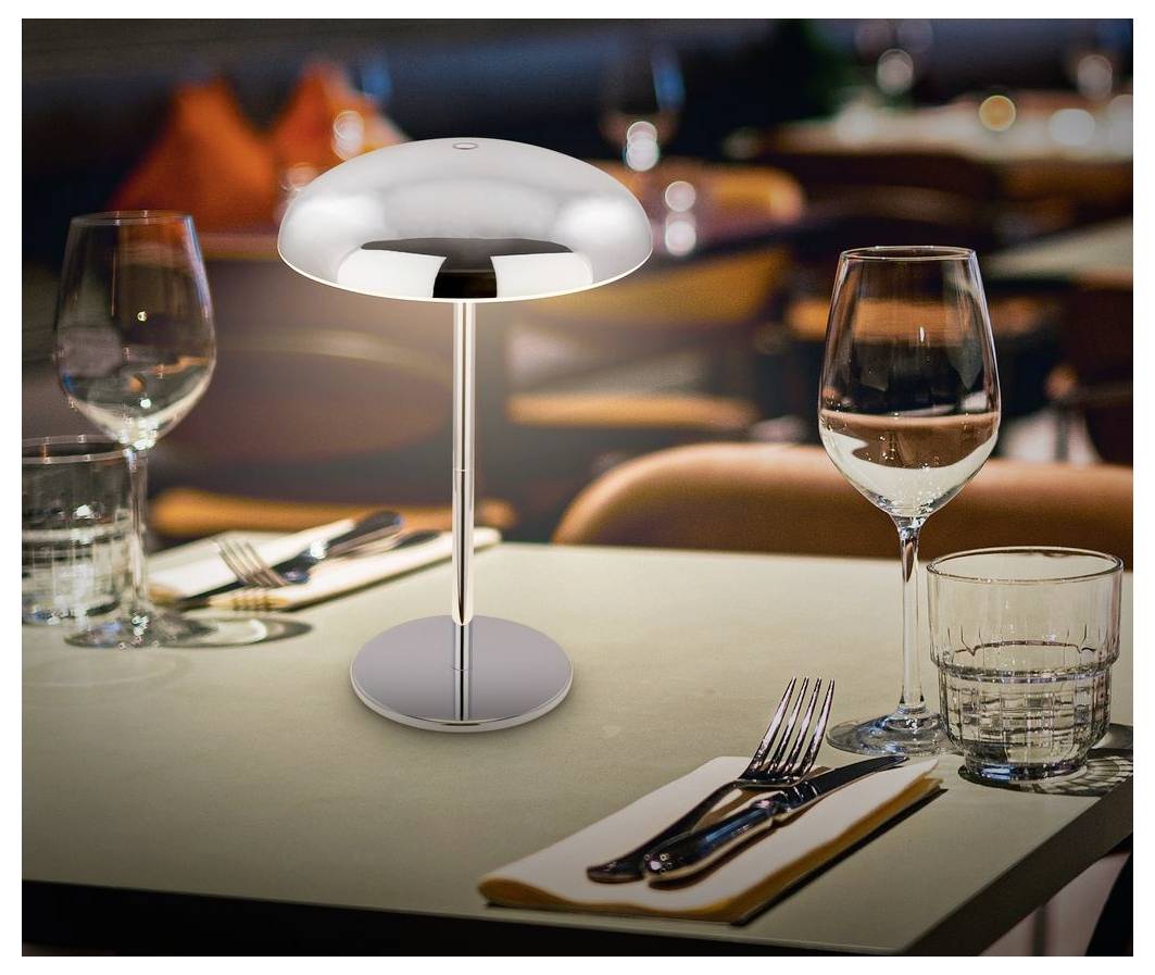 Moderne Tischleuchte auf einem Restauranttisch mit Weingläsern, Wasserglas und Besteck in einem sanft beleuchteten Esszimmer.