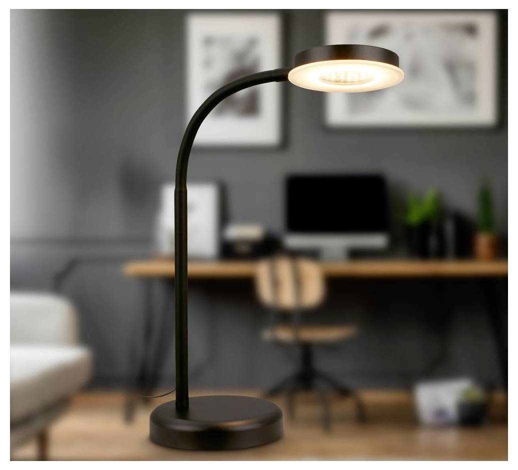 Schwarze Schreibtischlampe mit leuchtendem rundem Kopf auf rundem Sockel, gezeigt in einem unscharfen Homeoffice mit Schreibtisch und Stuhl dahinter.