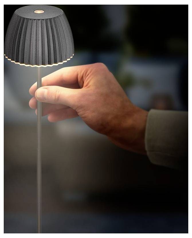 Hand passt eine kleine graue Lampe mit einem gefalteten Schirm an, was auf eine Tisch- oder Maßstabsmodell-Leuchte hindeutet.