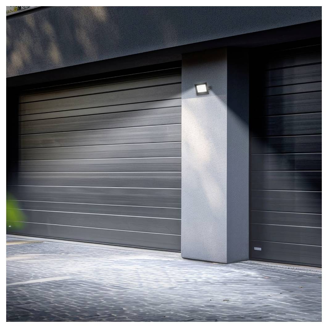 Modernes Hausäußeres mit zwei dunklen Garagentoren und einer beleuchteten wandmontierten Leuchte auf einer zentralen Säule, von der Auffahrt aus betrachtet.
