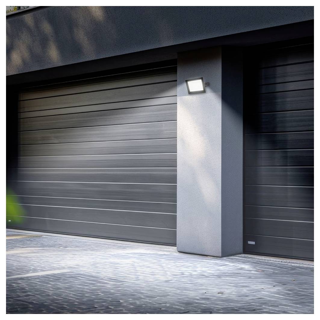 Modernes Hausäußeres mit zwei dunkelgrauen Garagentoren und einer wandmontierten Leuchte auf einem zentralen Pfeiler, vom Eingangsbereich aus betrachtet.