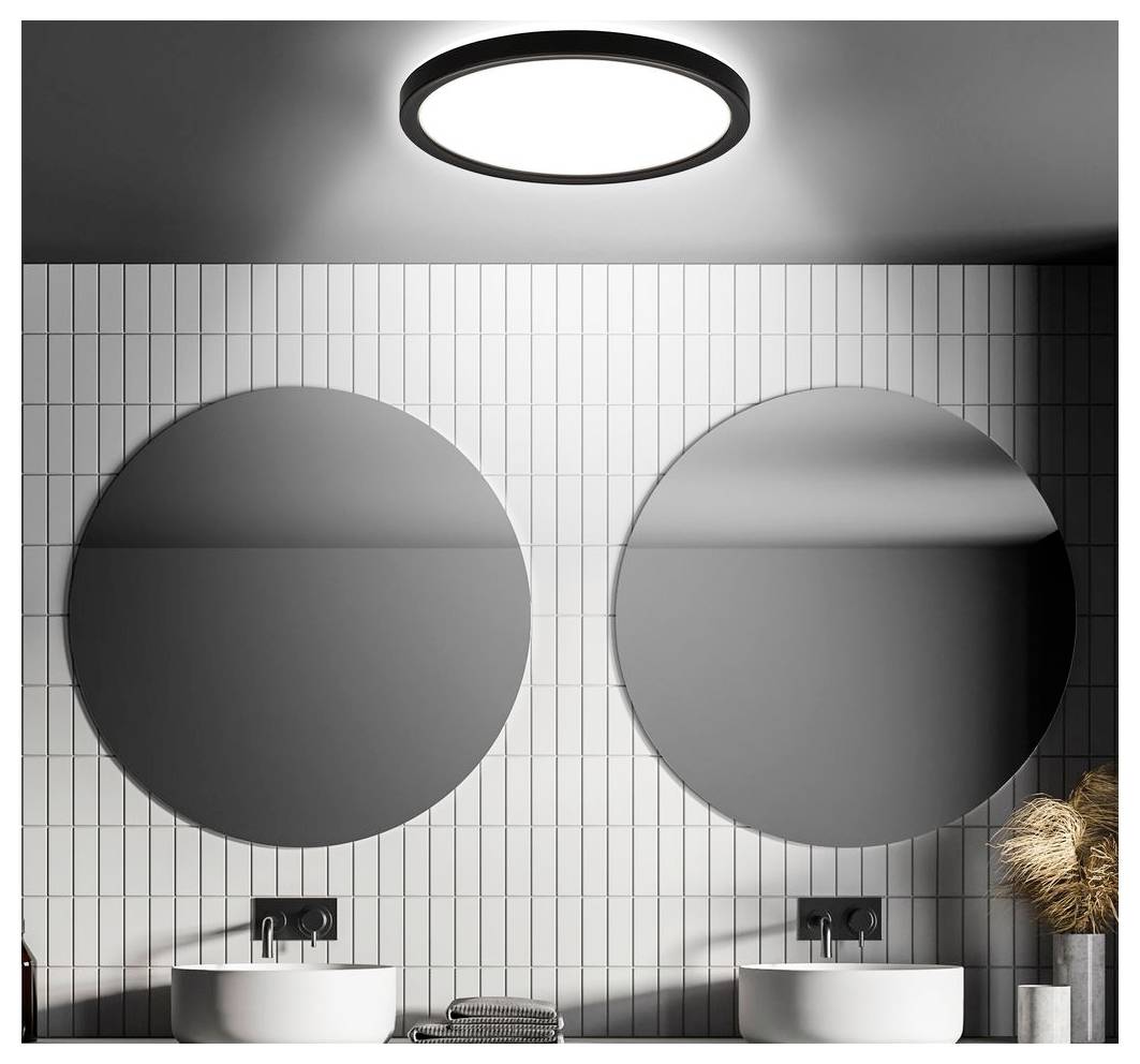 Modernes Badezimmer mit zwei runden Wandspiegeln über doppelten Aufsatzwaschbecken auf einer gefliesten Wand, beleuchtet durch eine runde Deckenleuchte.