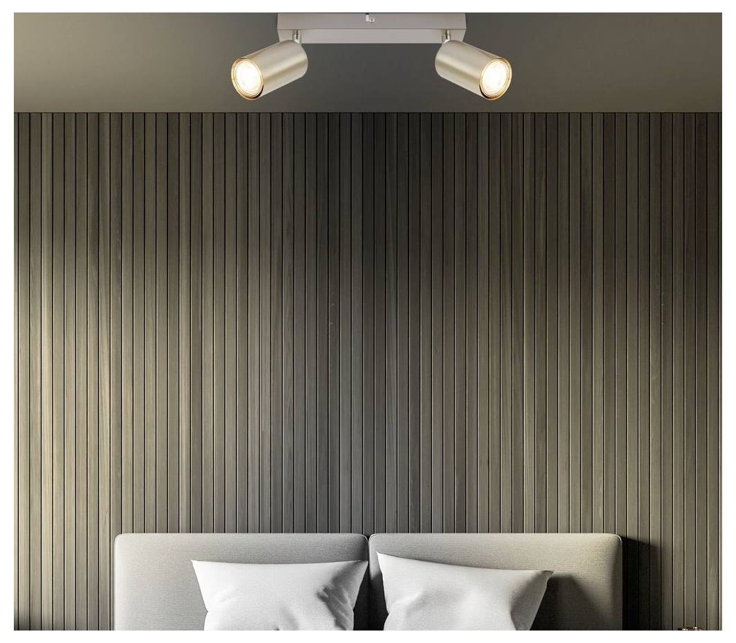 Modernes Schlafzimmer mit einem grau gepolsterten Bett und Kissen vor einer vertikal lamilierten dunklen Wand, beleuchtet durch zwei Deckenspots.