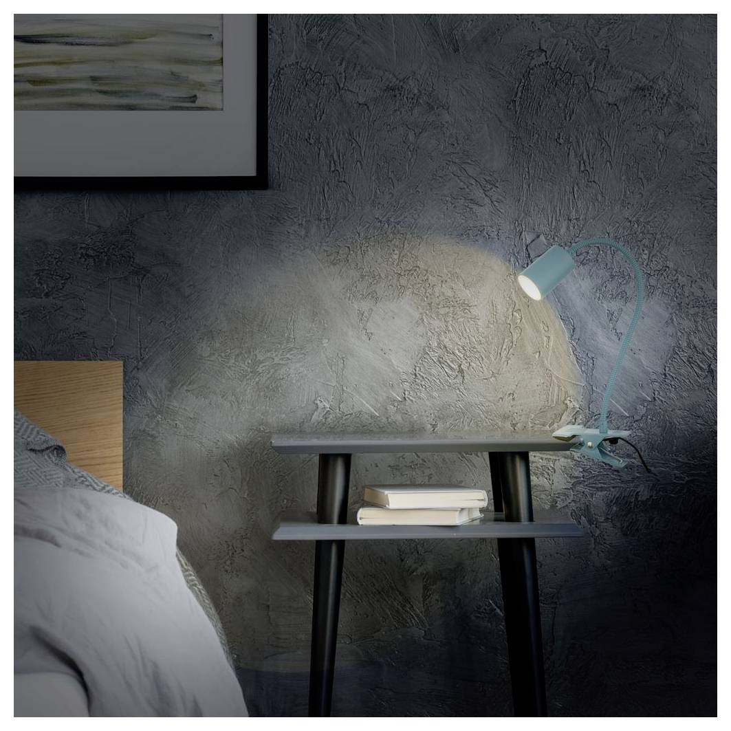 Nachttisch mit türkisfarbener Lampe, die Licht auf eine strukturierte Wand wirft, neben einem Bett mit Kissen und Büchern darunter.