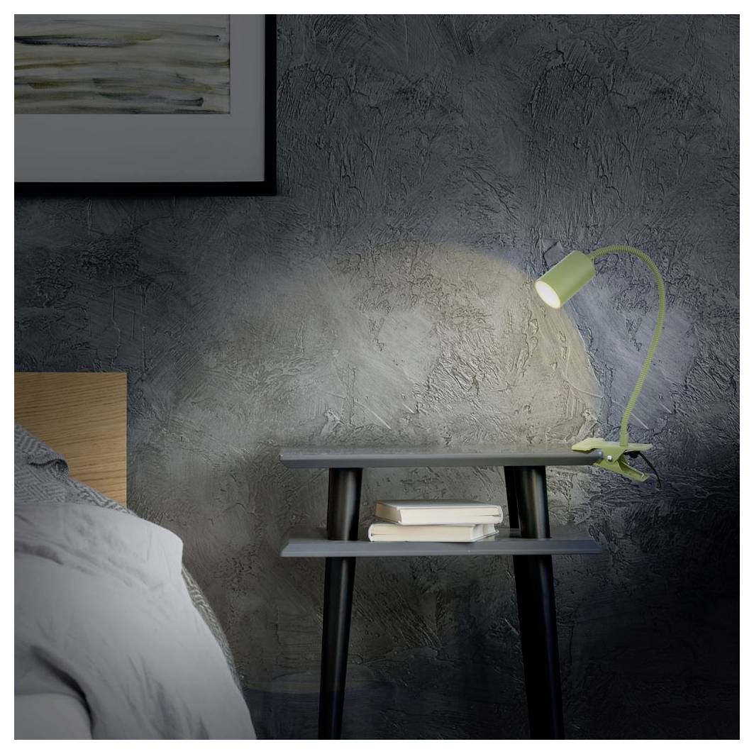 Ein Nachttisch mit einer grünen Lampe und Büchern neben einem Bett an einer dunkel strukturierten Wand.