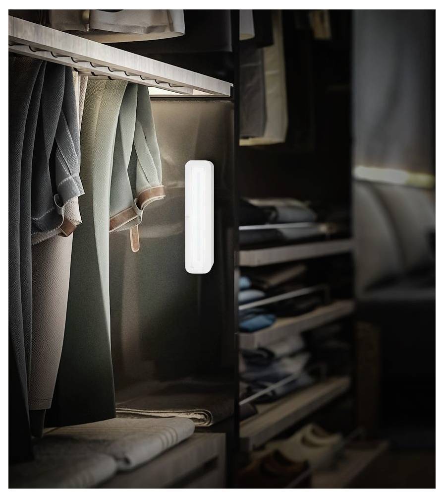 Ein offener Kleiderschrank mit hängenden Kleidern und gefalteten Gegenständen, beleuchtet durch ein kleines weißes Bewegungsmelder-Licht an der Türzarge.