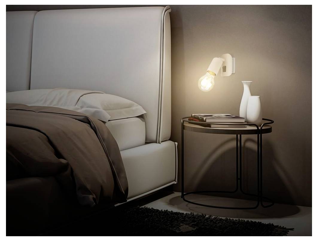 Gemütliche Schlafzimmerecke mit gepolstertem Bett, zerwühlter Bettwäsche, Nachttisch, beleuchtete Wandleuchte und weiße Vasen vor einer dunklen Wand.