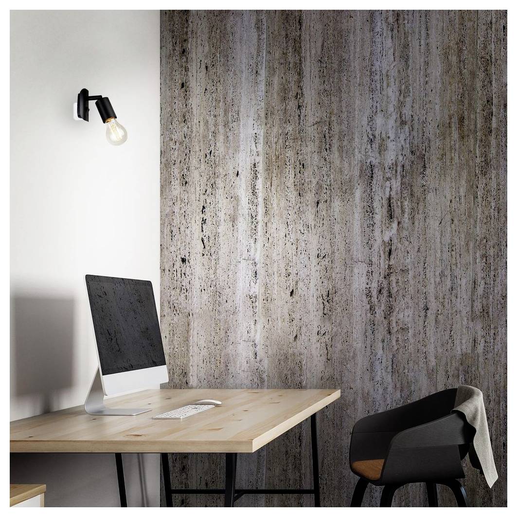 Modernes Schreibtischset mit Desktop-Computer, Tastatur und Stuhl vor einer strukturierten Wand, beleuchtet durch eine einzelne wandmontierte Lampe.