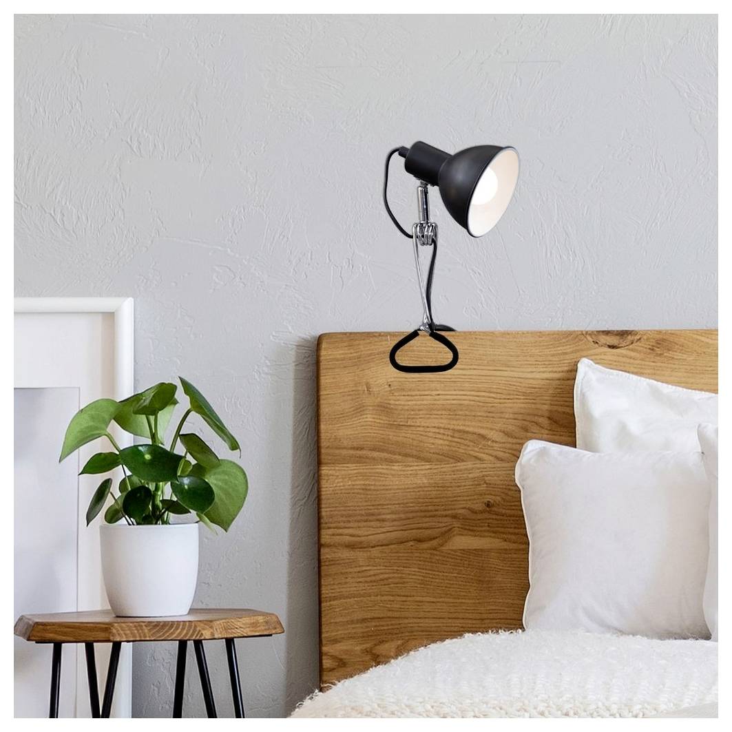 Minimalistisches Schlafzimmerecke mit hölzernem Kopfteil, beleuchteter schwarzer Wandleuchte, weißen Kissen, Topfpflanze und an der Wand lehnender Bilderrahmen.