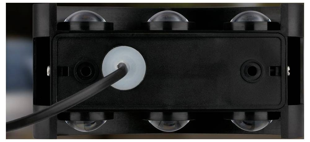 Nahaufnahme eines schwarzen Gerätepanels mit einem in einen linken Anschluss gesteckten Kabel, das von kreisförmigen Halterungen gehalten wird, wahrscheinlich ein Stecker an einer Maschine oder Kameraanlage.