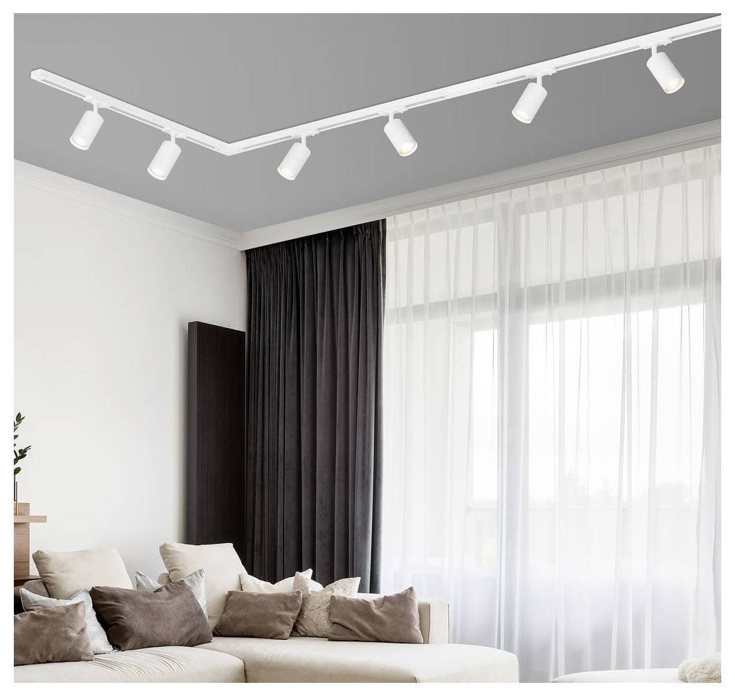 Modernes Wohnzimmer mit einem L-förmigen Ecksofa, gestaffelten beige- und braunen Kissen, raumhohen Vorhängen und Decken-Schienenstrahler.