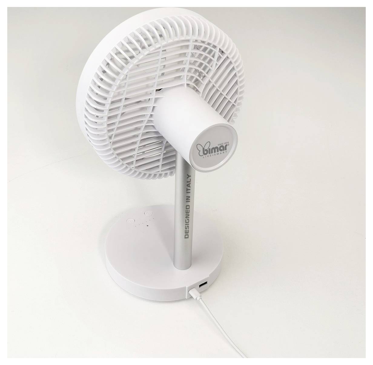 Weißer Tischventilator mit rundem Sockel, neigbarem Kopf und sichtbarem Stromkabel auf einfachem Hintergrund.