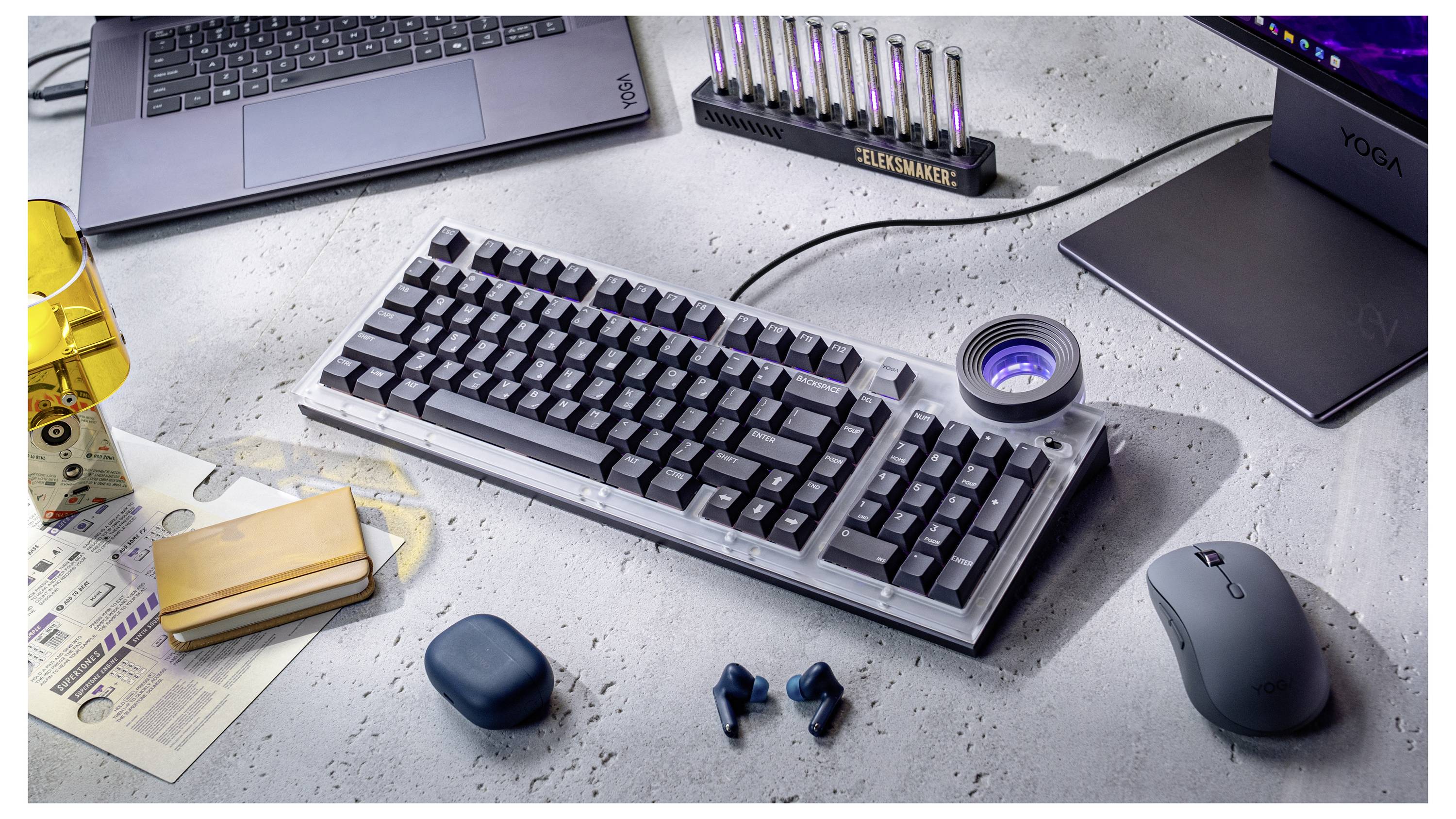 Eine mechanische Tastatur auf einem Schreibtisch mit einem Laptop, einer kabellosen Maus, Ohrhörern und kleinen technischen Zubehörteilen herum.