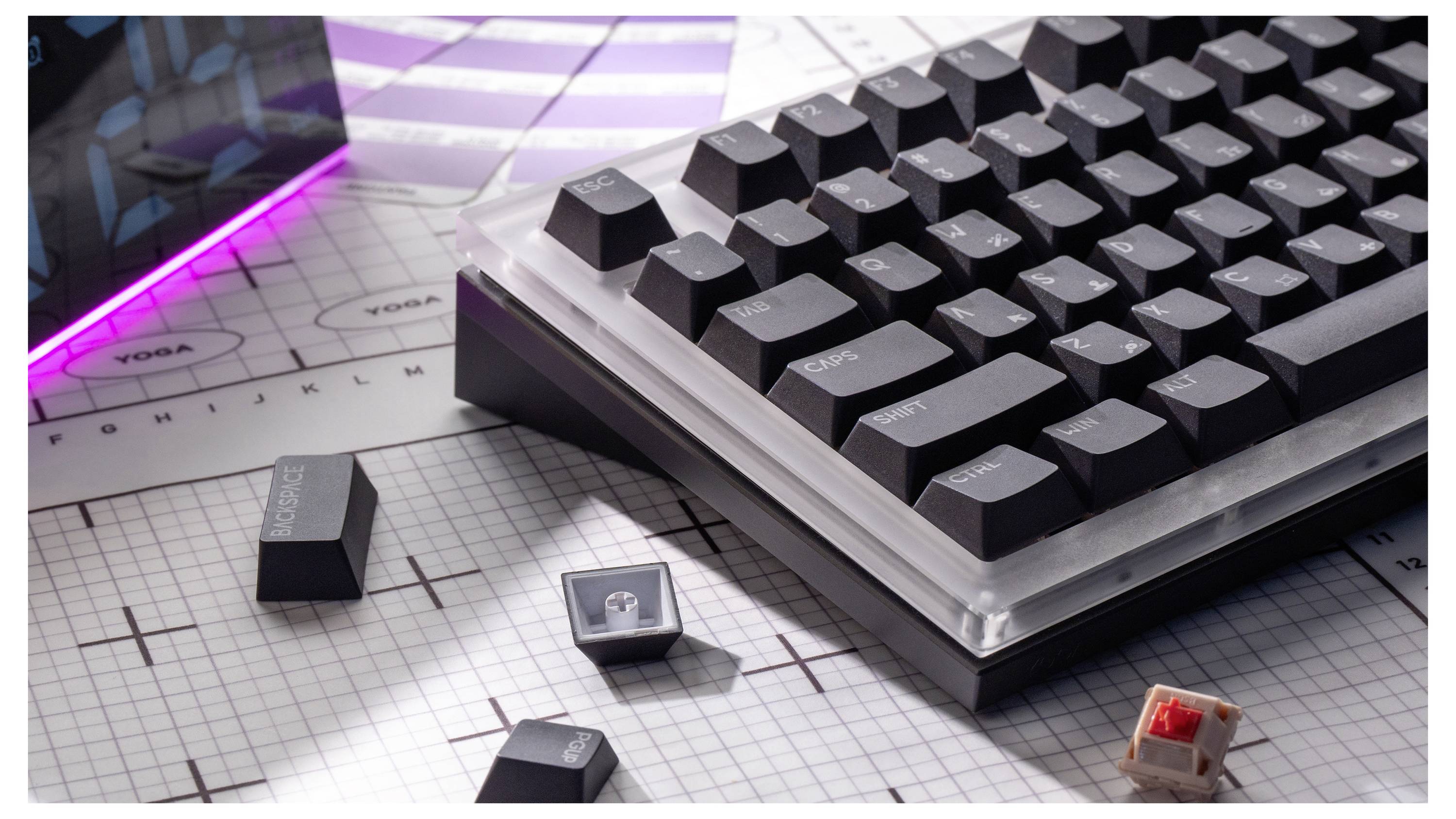 Nahaufnahme einer mechanischen Tastatur auf einem karierten Schreibtisch mit verstreuten Tasten, einschließlich einer roten Schalter-Taste, unter purpurnem Umgebungslicht.