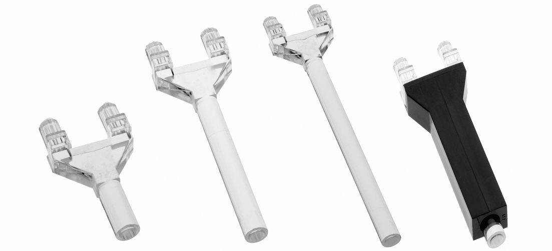 Vier handgehaltene Kosmetik-Applikatoren mit doppelten durchsichtigen kammartigen Köpfen, gezeigt in weißem und schwarzem Kunststoff auf einfachem Hintergrund.