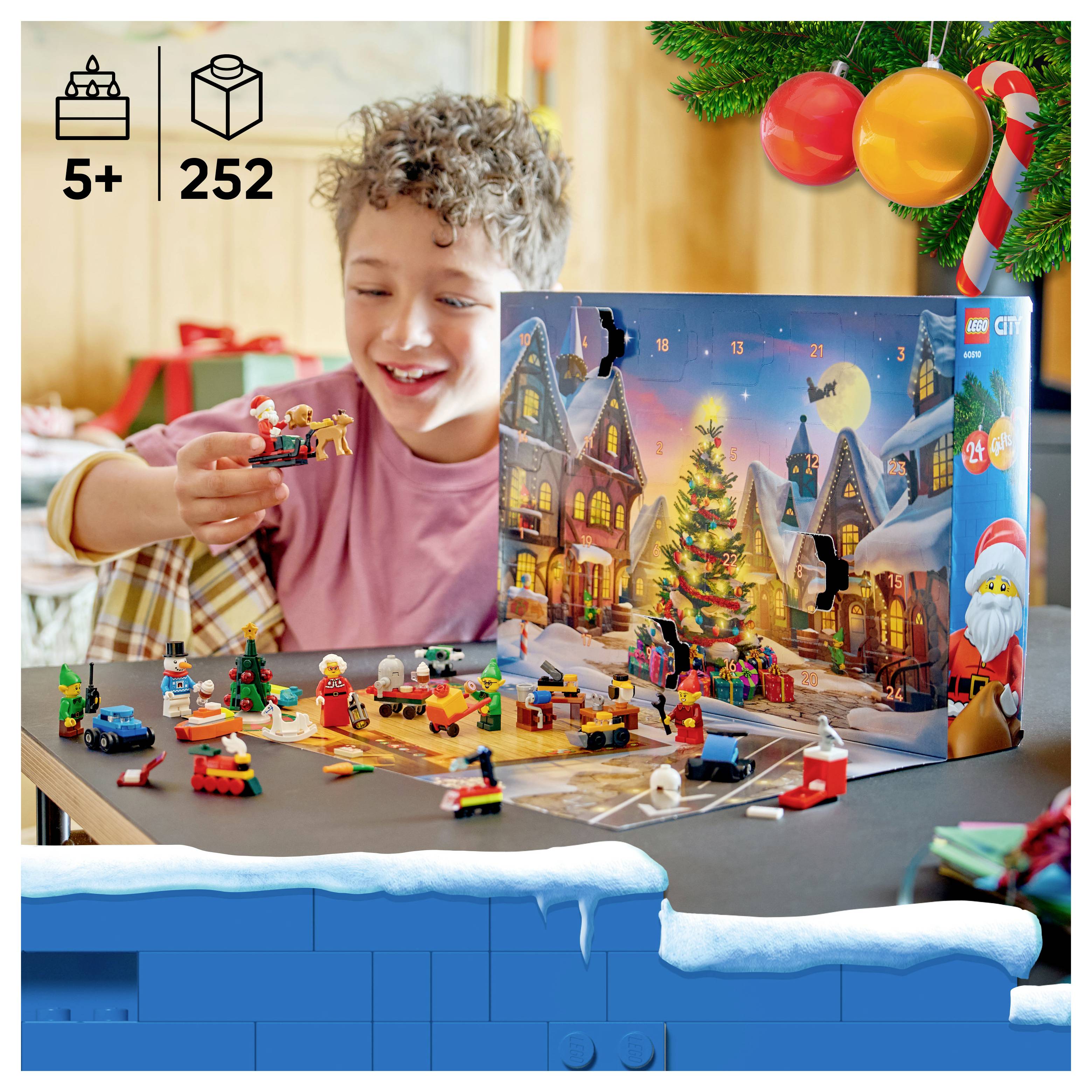 Kind öffnet einen LEGO City Adventskalender mit Altersempfehlung ab 5 Jahren und 252 Teilen, hält eine kleine Spielfigur in der Hand, während verstreute Miniaturbauten auf einem festlichen Tisch verteilt sind.