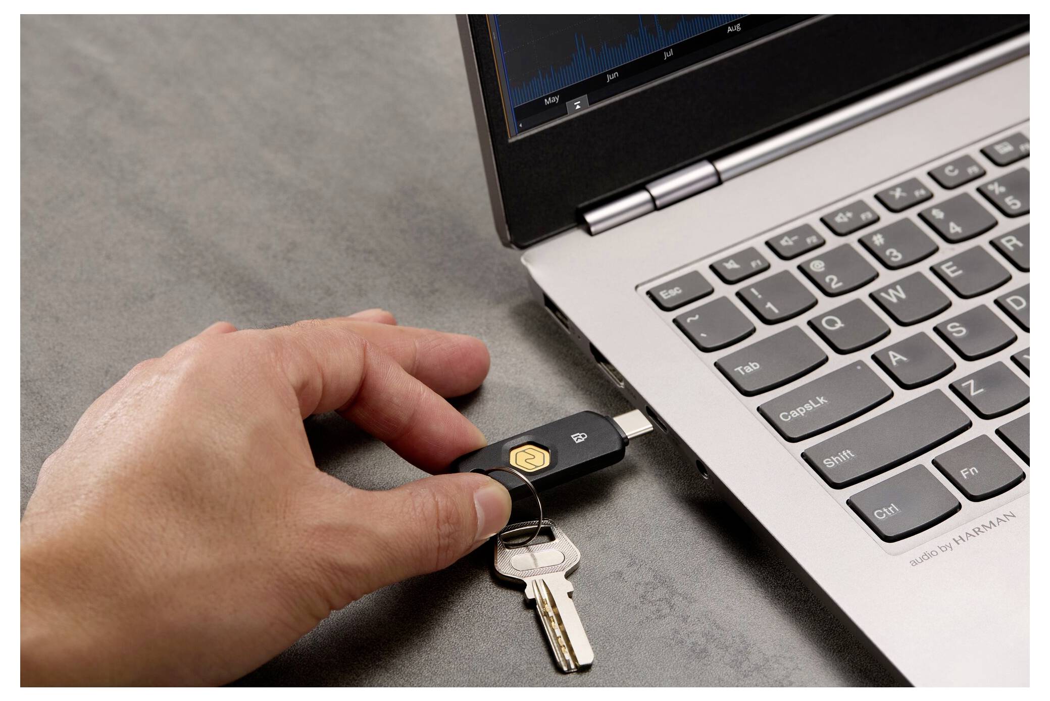 Hand, die einen USB-Sicherheitsschlüssel in einen Laptop einsteckt, mit zwei Schlüsseln auf einem Schlüsselring in der Nähe.
