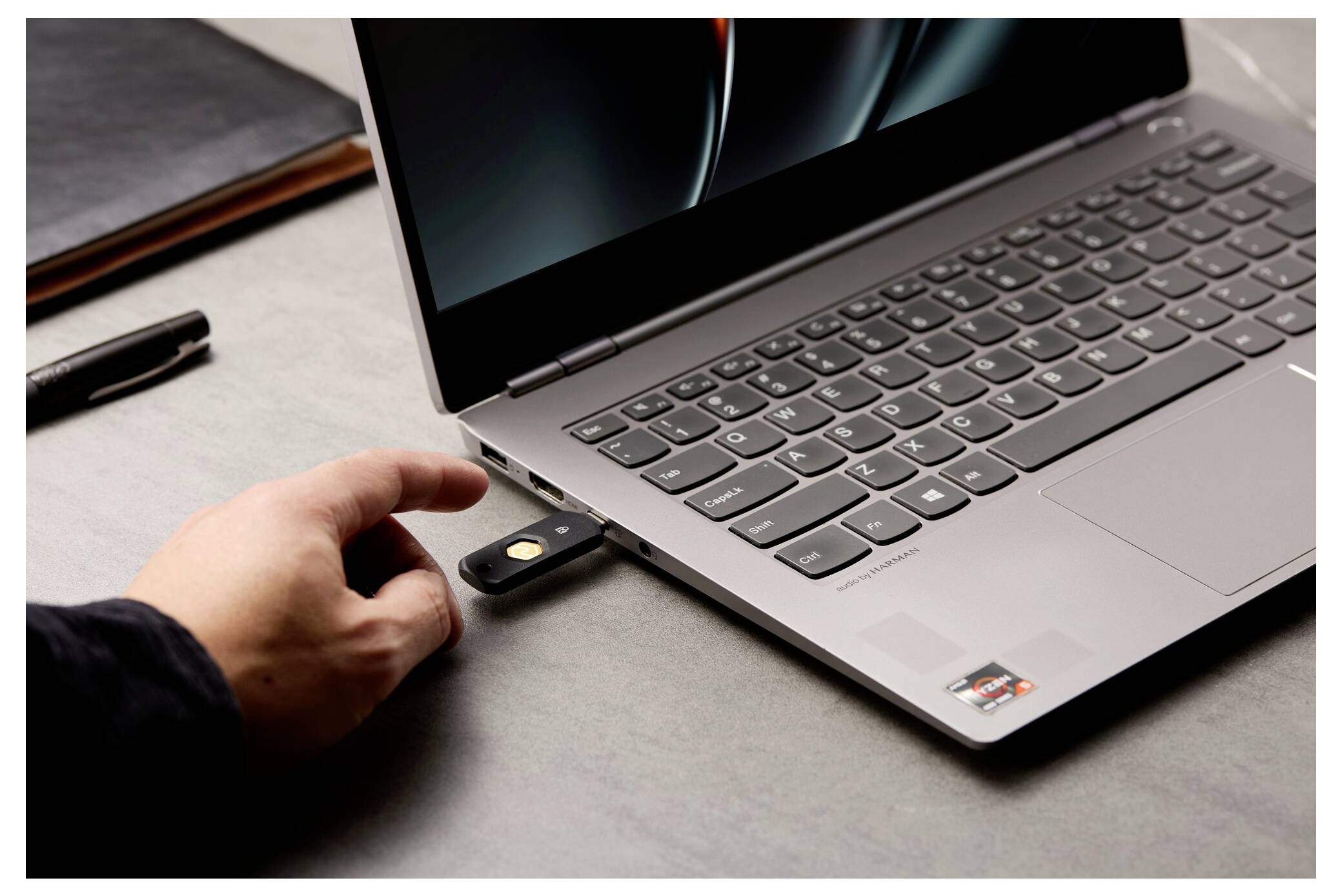 Eine Person steckt einen USB-Sicherheitsschlüssel in einen Laptop auf einem Schreibtisch, was auf eine Zwei-Faktor- oder Hardware-Authentifizierung hindeutet.