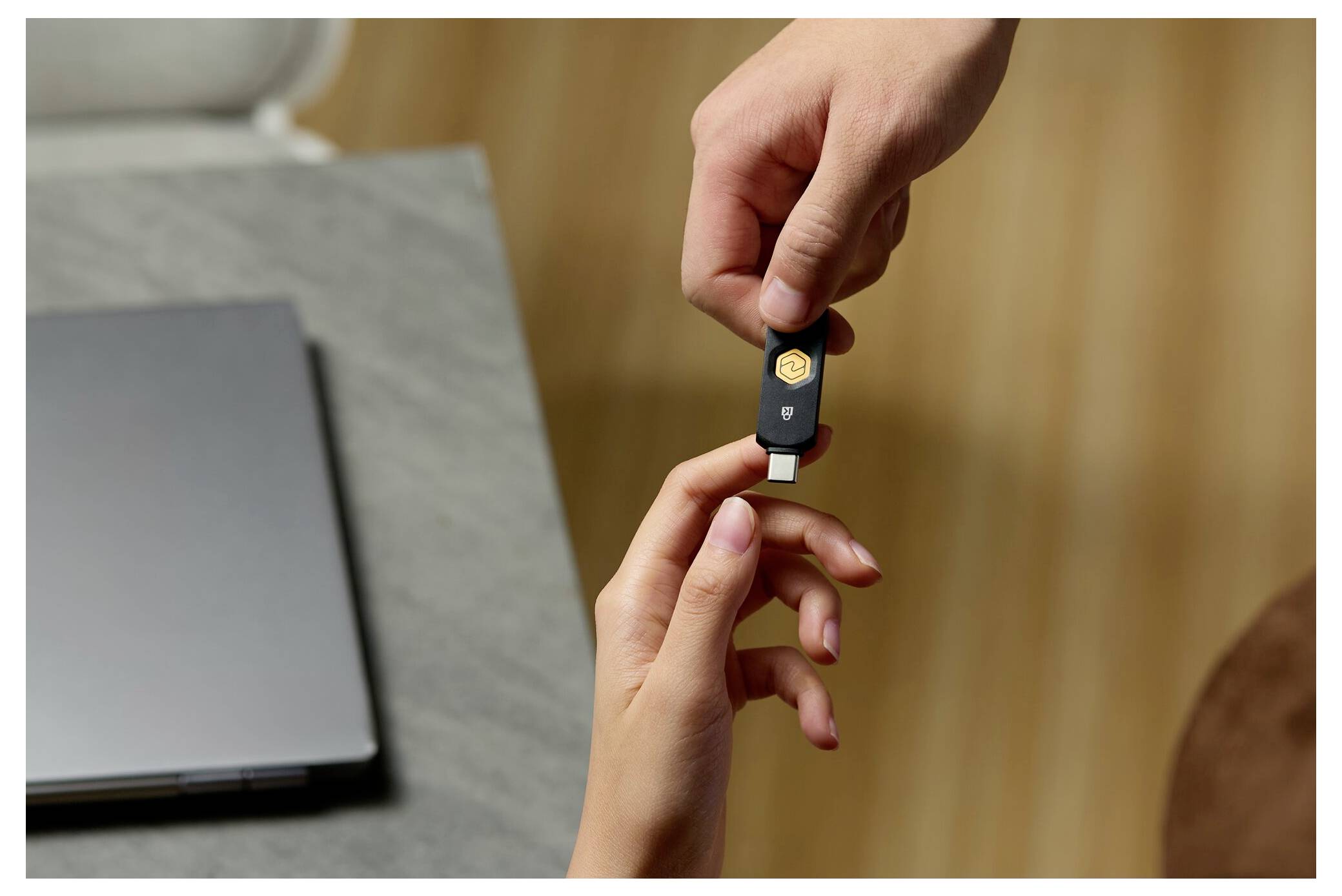 Hände, die einen USB-Sicherheitsschlüssel neben einem Laptop austauschen, was auf Zwei-Faktor-Authentifizierung oder sichere Anmeldung hindeutet.