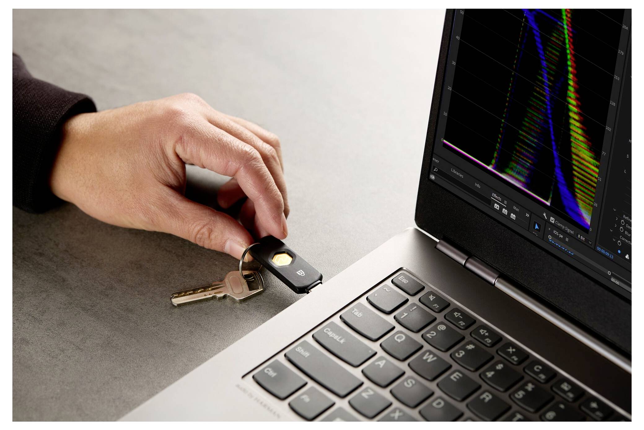 Eine Hand, die einen Autoschlüssel neben einen Laptop legt, auf dessen Bildschirm bunte Daten angezeigt werden, was auf digitale Autoschlüsselprogrammierung oder Sicherheitsanalyse hindeutet.