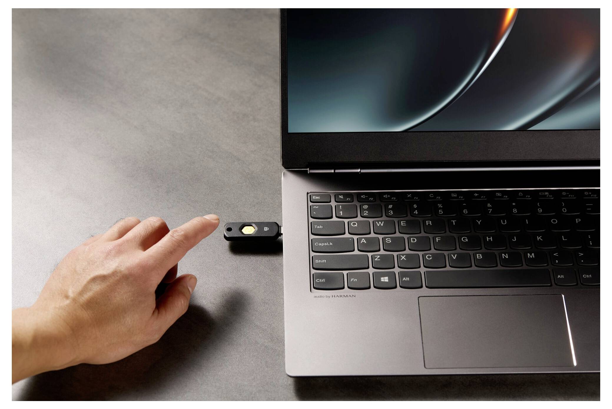 Hand, die einen USB-Stick in einen Laptop neben der Tastatur und dem Trackpad auf einem grauen Schreibtisch einsteckt.