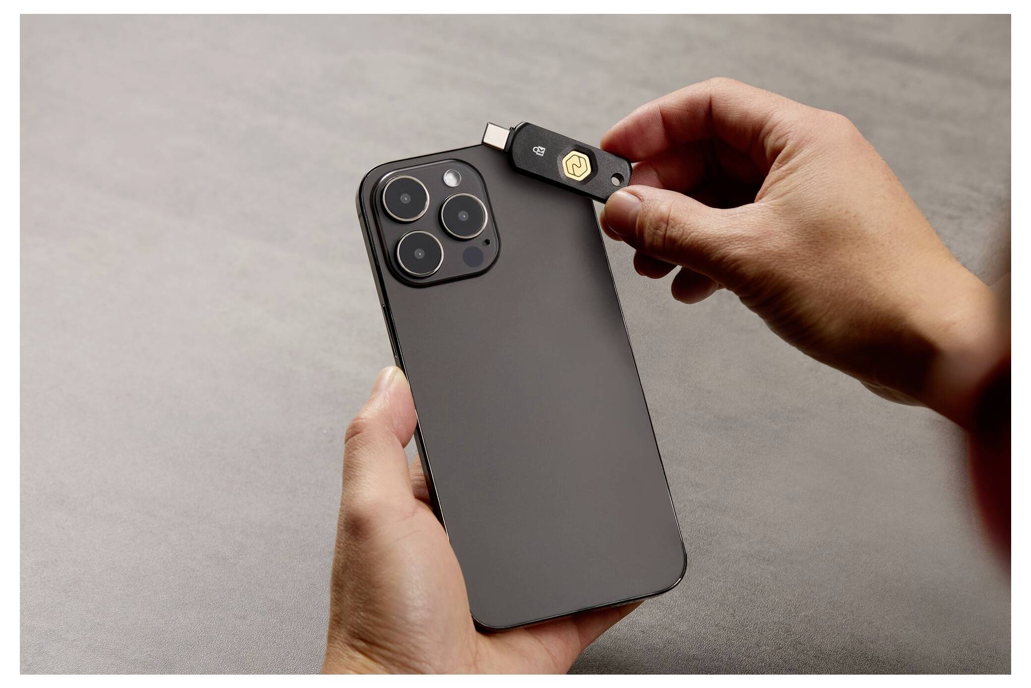 Hände führen einen USB-C-Sicherheitsschlüssel in die Oberseite eines schwarzen Smartphones ein, was auf Zwei-Faktor-Authentifizierung oder Geräteeinrichtung hindeutet.