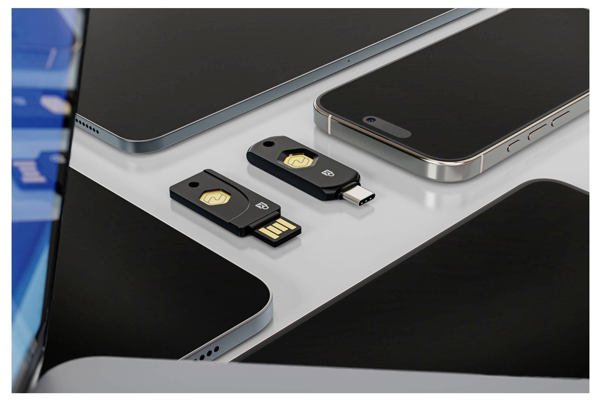 Zwei USB-Sicherheitsschlüssel, einer USB-A und einer USB-C, zwischen mehreren Smartphones auf einem Tisch platziert.