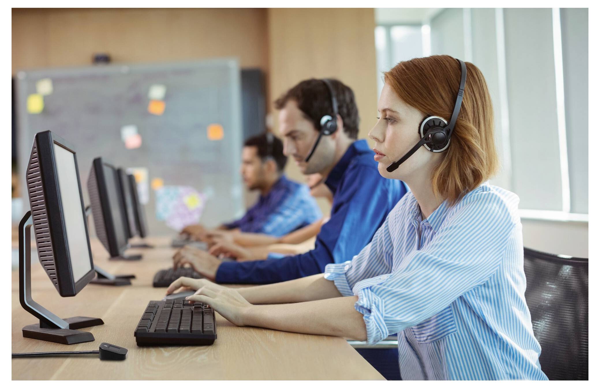 Drei Kundendienstmitarbeiter mit Kopfhörern arbeiten an Desktop-Computern in einem Callcenter.
