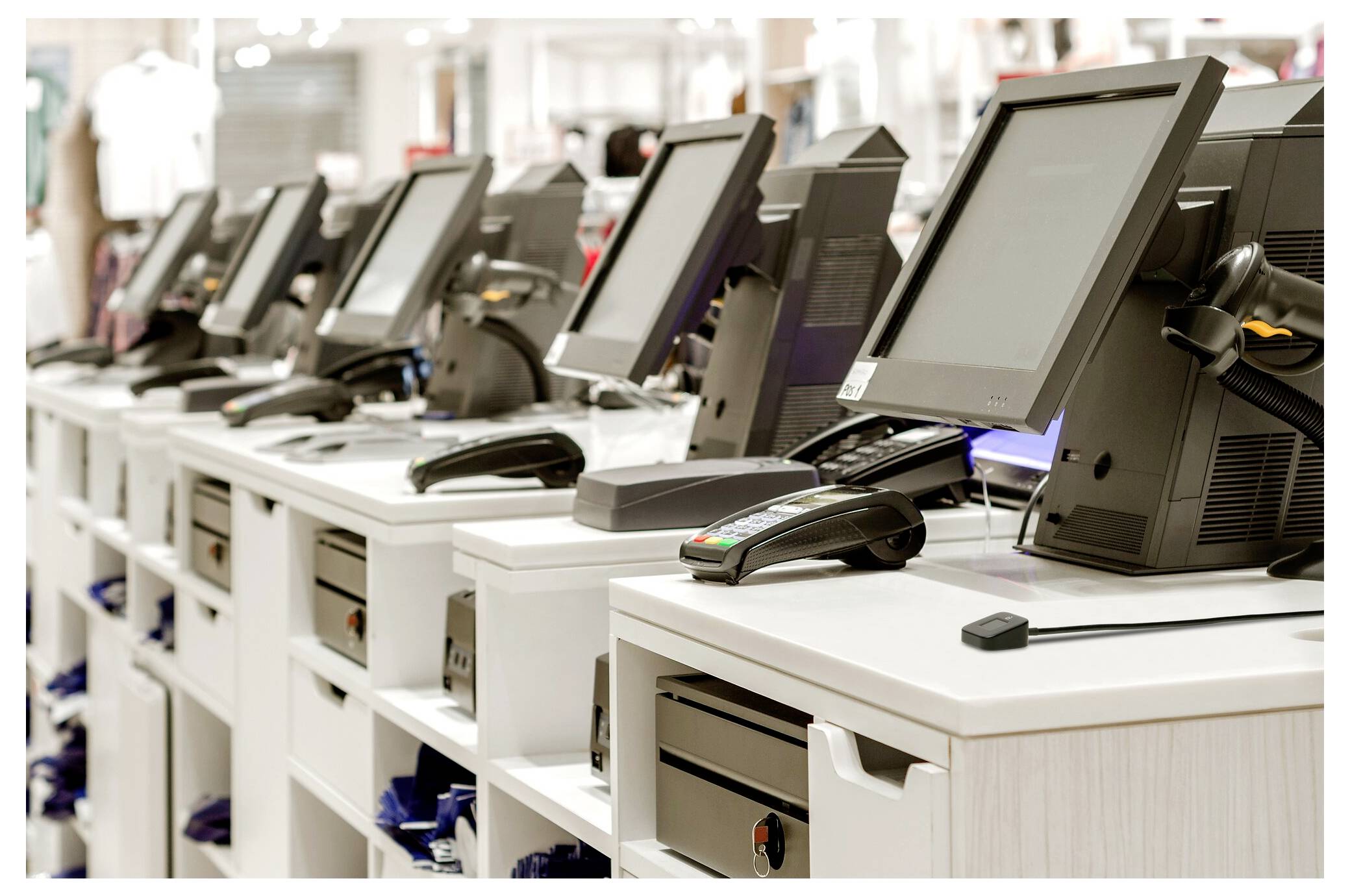 Reihe von Point-of-Sale-Touchscreen-Terminals mit Kartenlesegeräten auf weißen Einzelhandels-Kassentheken in einem Geschäft.
