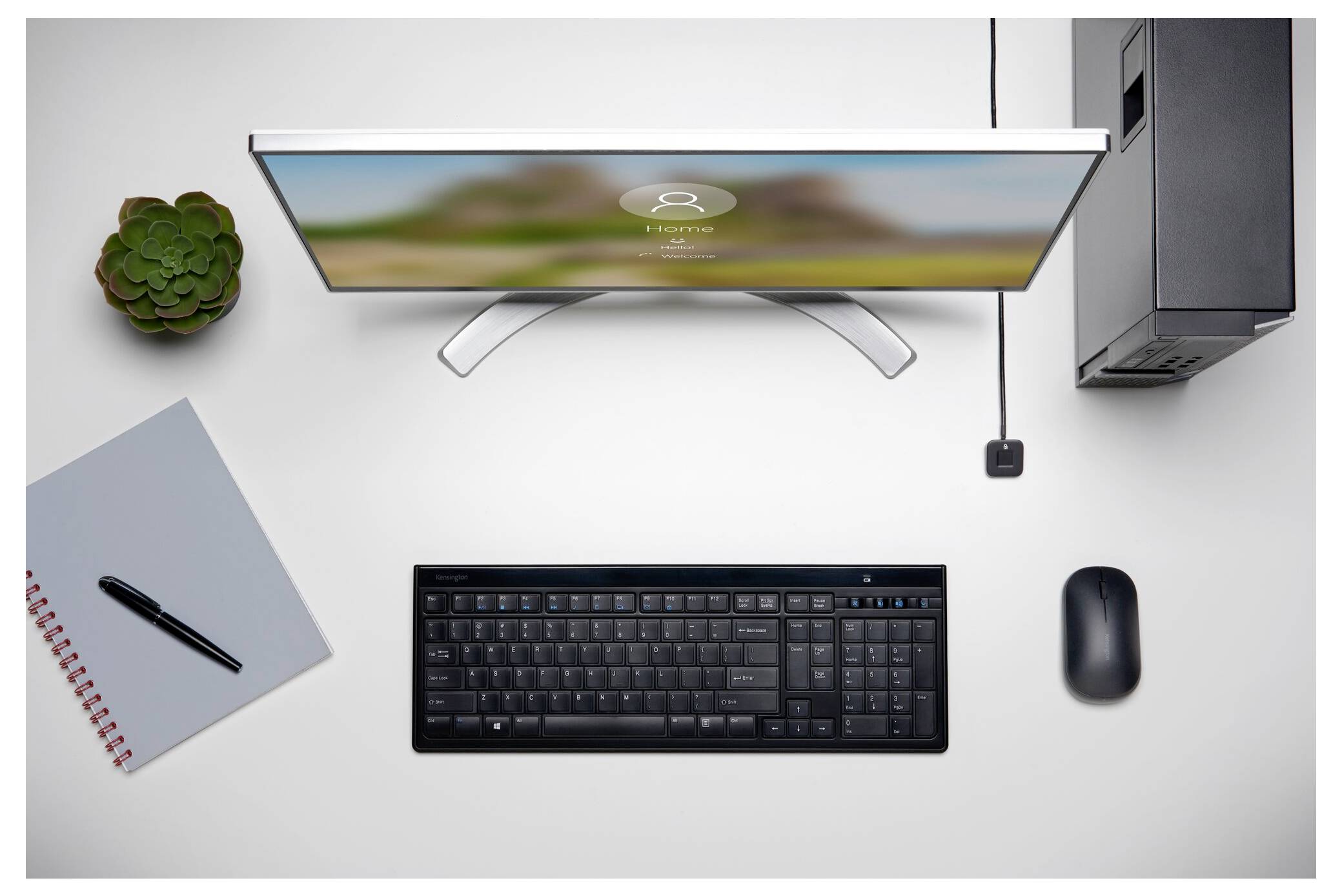 Draufsicht auf einen minimalistischen Schreibtisch mit einem Monitor, einer Tastatur, einer Maus, einem Notizbuch und einem Stift, einem Computerturm, einer Steckdose und einer Topfpflanze.