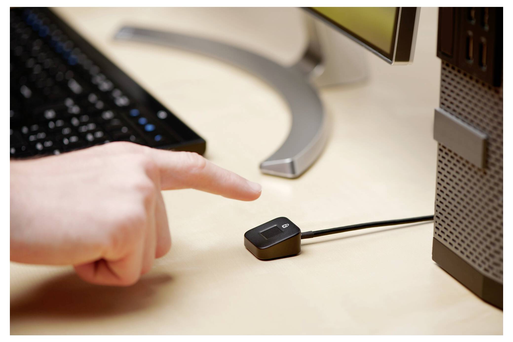 Hand pointing at a small black USB-Gerät, das an einen Desktop-Computer auf einem Schreibtisch angeschlossen ist.