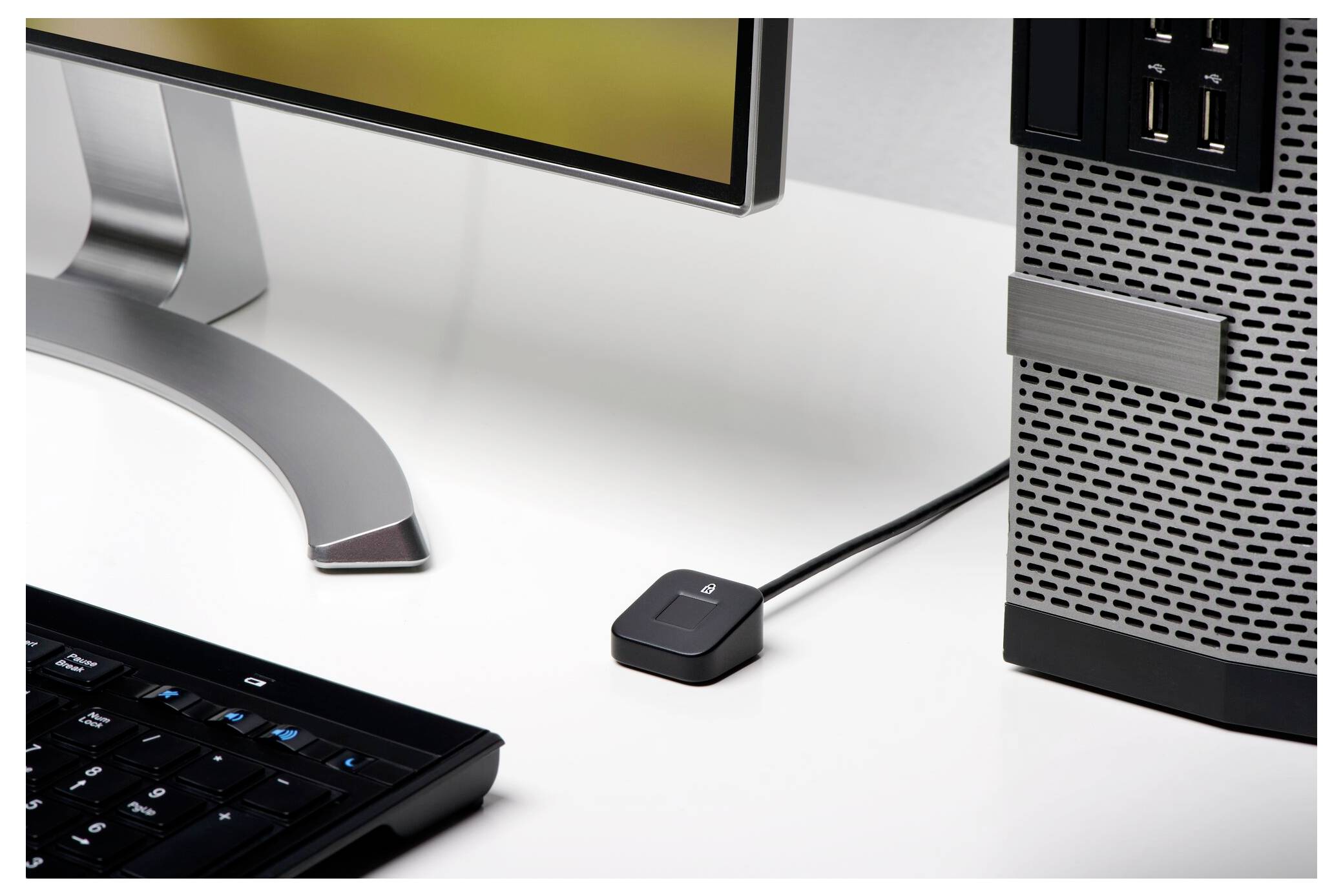 Eine Desktop-Computer-Einrichtung mit Monitor, Tastatur und Gehäuse; ein kleines schwarzes Kabelgerät sitzt auf dem Schreibtisch neben dem Gehäuse.